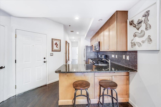 kitchen with kitchen peninsula, decorative backsplash, dark stone countertops, and appliances with stainless steel finishes