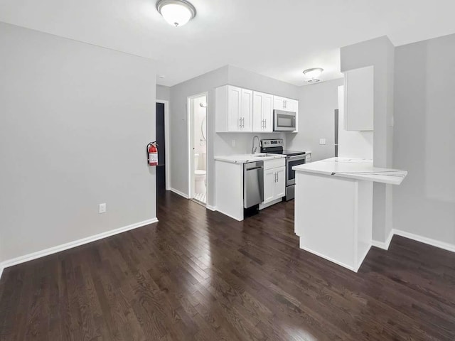 kitchen with dark wood-type flooring, white cabinetry, kitchen peninsula, and stainless steel appliances