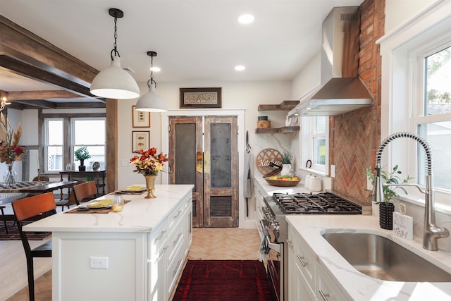 kitchen featuring high end range, wall chimney exhaust hood, decorative light fixtures, white cabinets, and a center island