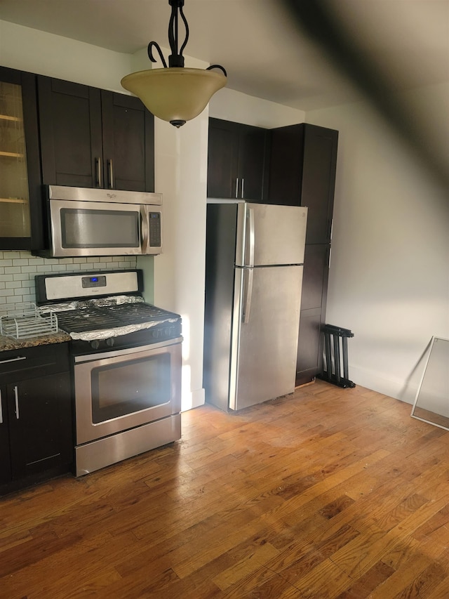 kitchen featuring dark stone counters, decorative backsplash, light wood-type flooring, and appliances with stainless steel finishes