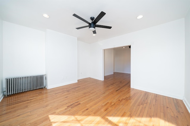 unfurnished room with ceiling fan, radiator heating unit, and light wood-type flooring