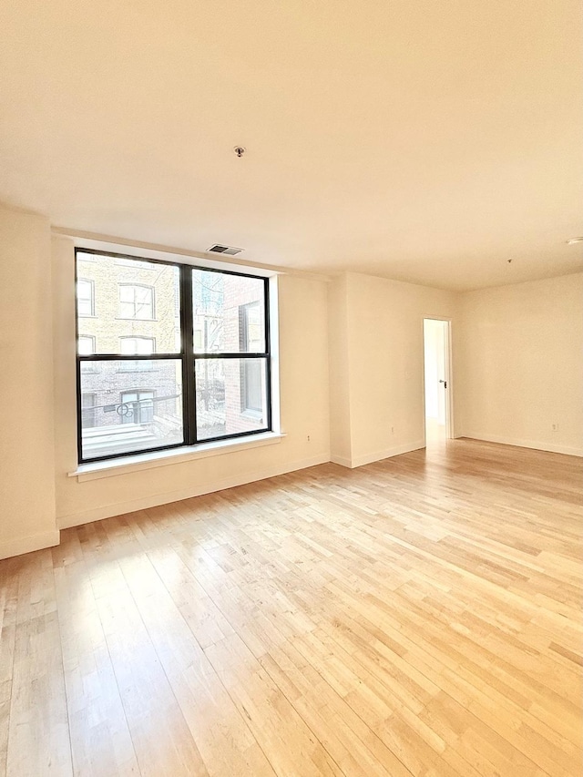 empty room with light wood-style floors, visible vents, and baseboards