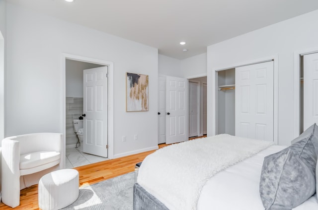 bedroom with baseboards, ensuite bath, recessed lighting, light wood-style floors, and multiple closets