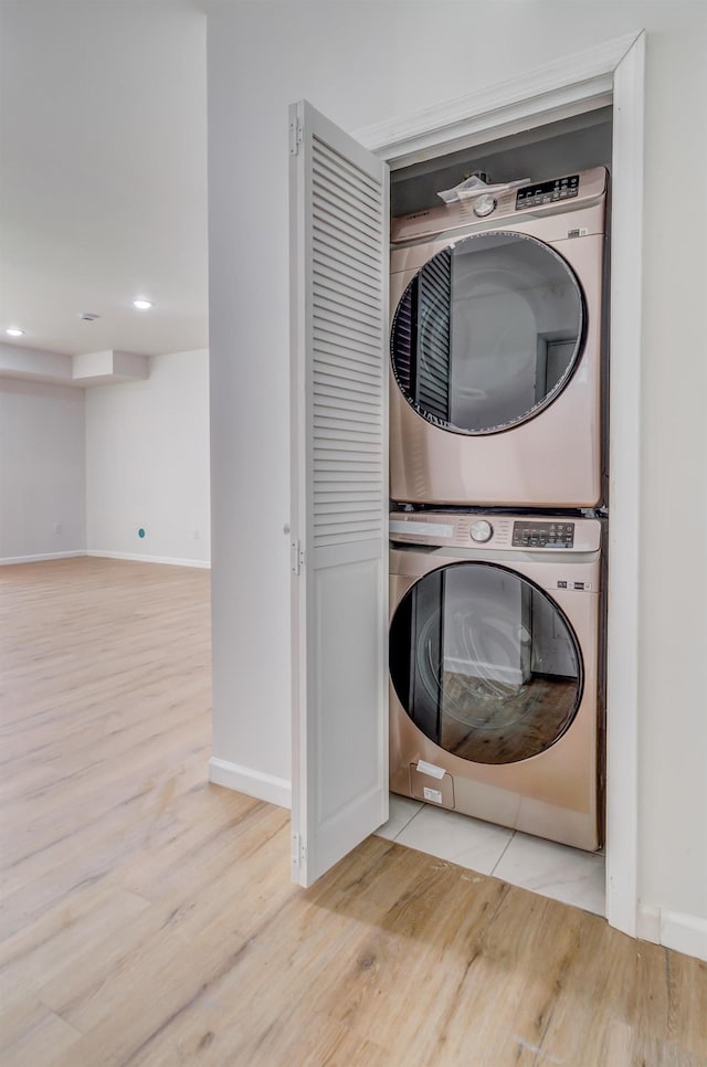 clothes washing area with stacked washer and clothes dryer, wood finished floors, recessed lighting, baseboards, and laundry area