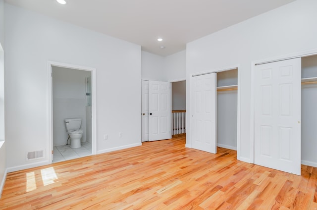 unfurnished bedroom with wood finished floors, baseboards, visible vents, two closets, and connected bathroom