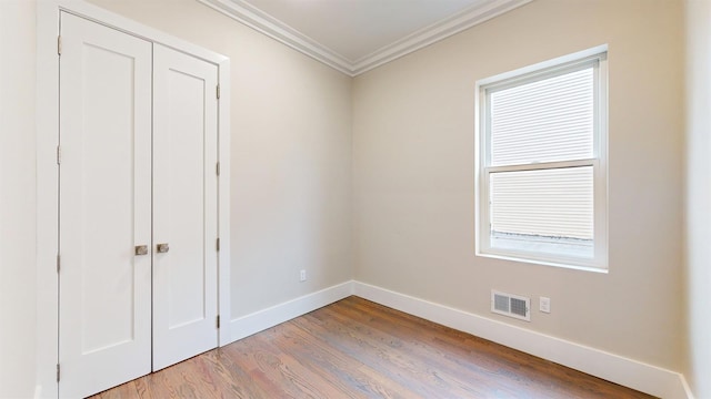 unfurnished bedroom featuring a closet, wood finished floors, baseboards, visible vents, and ornamental molding