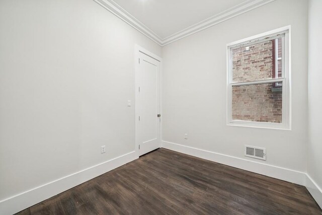 empty room featuring baseboards, dark wood-style flooring, ornamental molding, and visible vents