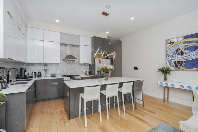 kitchen featuring decorative light fixtures, a center island, appliances with stainless steel finishes, wall chimney range hood, and white cabinets