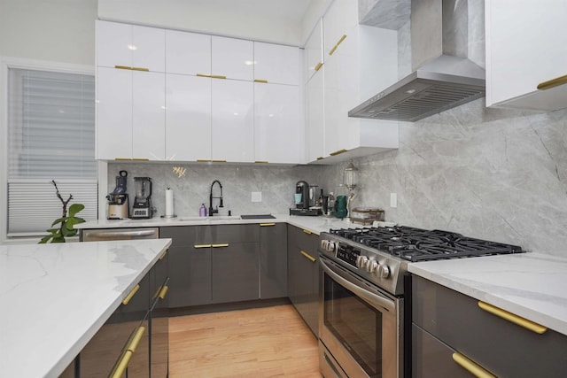 kitchen with white cabinetry, wall chimney range hood, stainless steel gas range oven, and light stone countertops