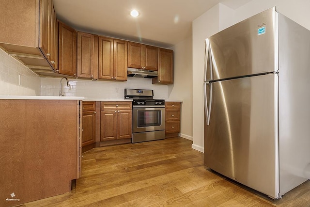 72 W 22nd St, Bayonne, NJ 07002 - kitchen featuring stainless steel appliances, under cabinet range hood, light wood-style flooring, brown cabinetry, and backsplash