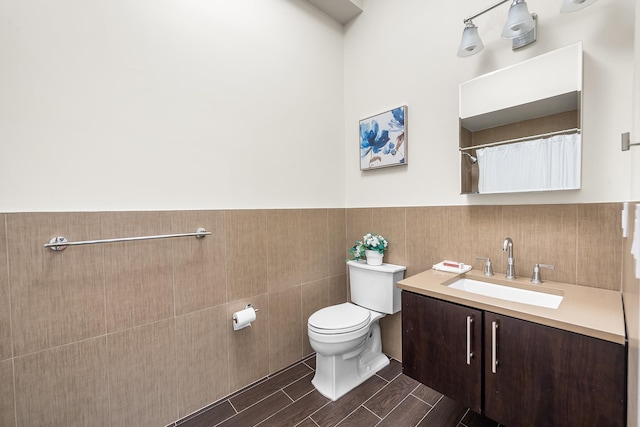 full bath featuring tile walls, toilet, vanity, a wainscoted wall, and wood finish floors
