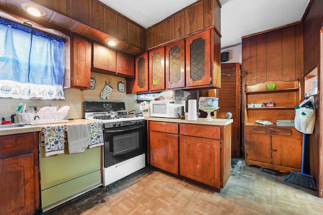 kitchen with light floors, light countertops, white microwave, glass insert cabinets, and gas range