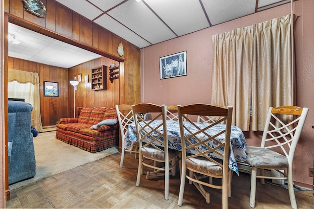 dining room with a drop ceiling, a baseboard radiator, and wooden walls