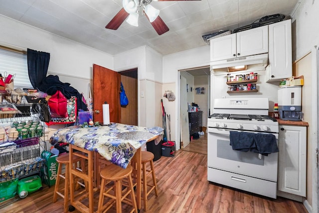 kitchen featuring ceiling fan, under cabinet range hood, white range with gas stovetop, wood finished floors, and white cabinetry