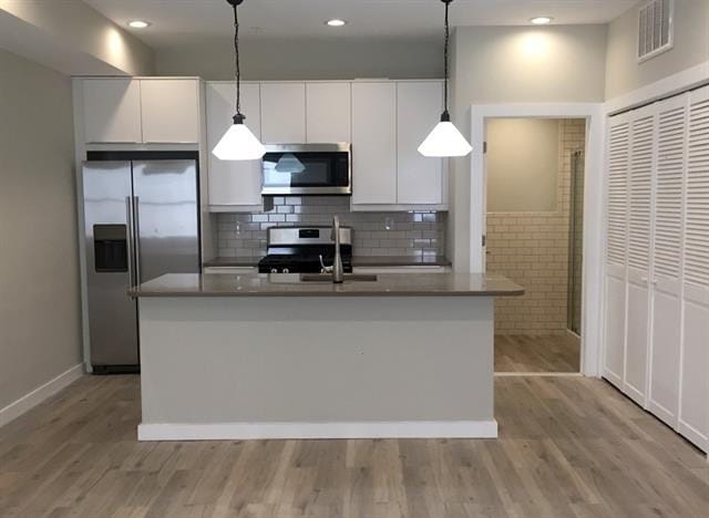 kitchen featuring white cabinetry, decorative light fixtures, a center island with sink, light hardwood / wood-style flooring, and stainless steel appliances