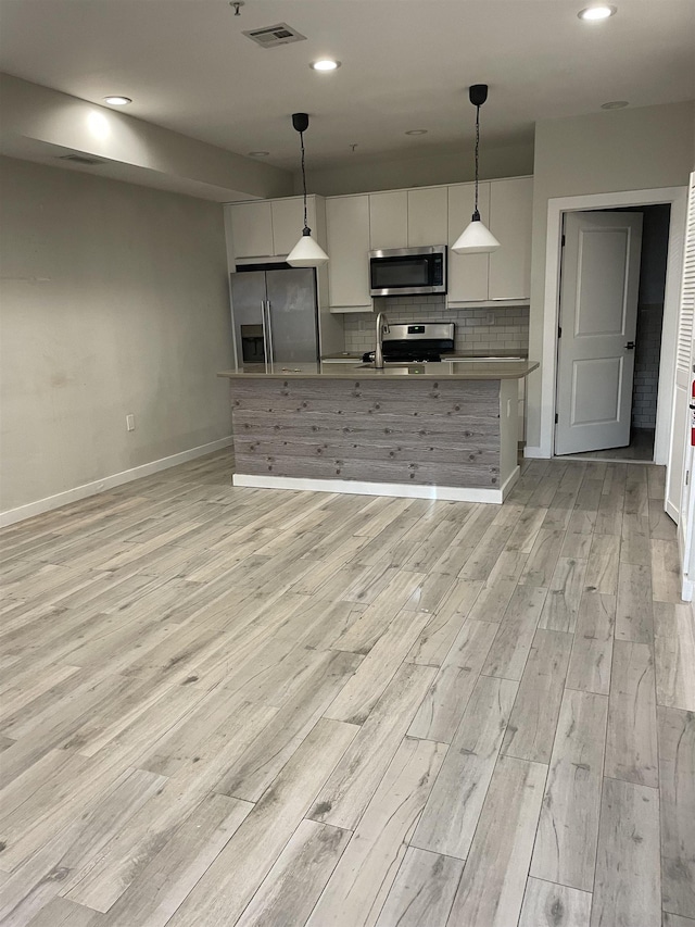 kitchen with appliances with stainless steel finishes, tasteful backsplash, white cabinetry, hanging light fixtures, and a kitchen island with sink