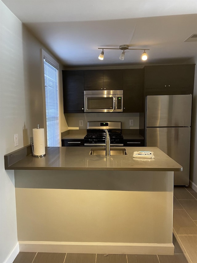 kitchen with appliances with stainless steel finishes, sink, light tile patterned floors, and kitchen peninsula