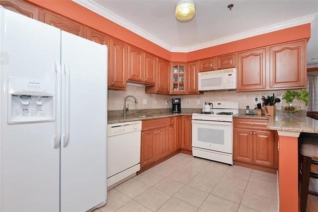 kitchen with white appliances, light stone counters, light tile patterned floors, ornamental molding, and a sink