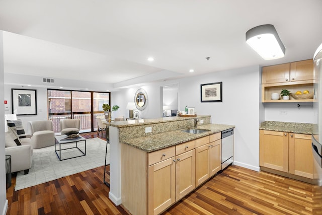 kitchen featuring light brown cabinets, a peninsula, a sink, open floor plan, and dishwasher