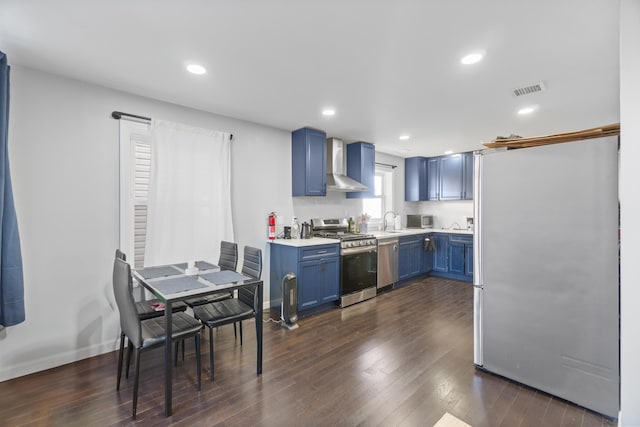225 Freeman Ave, Jersey City, NJ 07306 - kitchen with blue cabinetry, wall chimney range hood, dark wood finished floors, stainless steel appliances, and light countertops