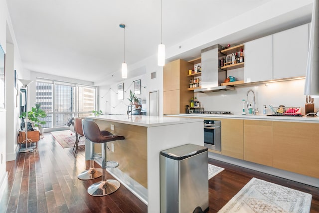 kitchen featuring dark wood-type flooring, stainless steel oven, decorative light fixtures, an island with sink, and expansive windows