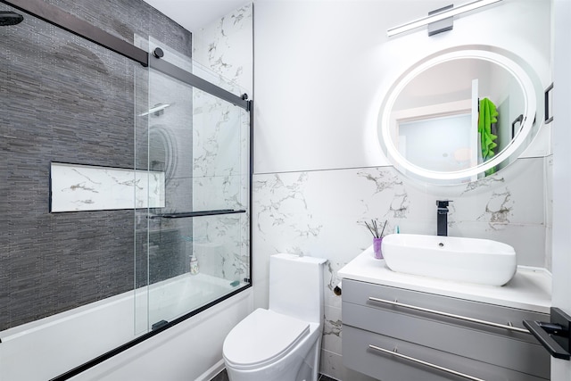 full bathroom featuring vanity, bath / shower combo with glass door, tile walls, and toilet