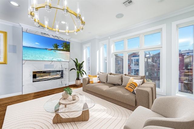 living room with hardwood / wood-style floors, ornamental molding, a high end fireplace, and a chandelier