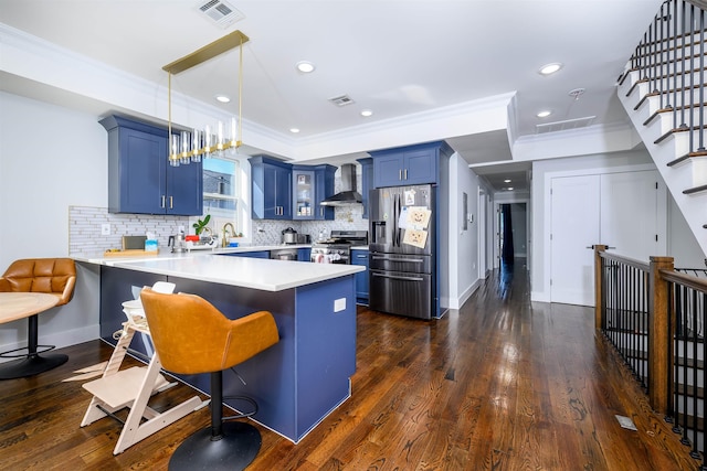 kitchen featuring wall chimney exhaust hood, blue cabinetry, a kitchen bar, kitchen peninsula, and stainless steel appliances