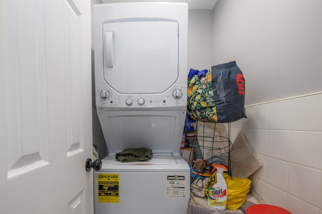 clothes washing area featuring stacked washer and dryer and tile walls