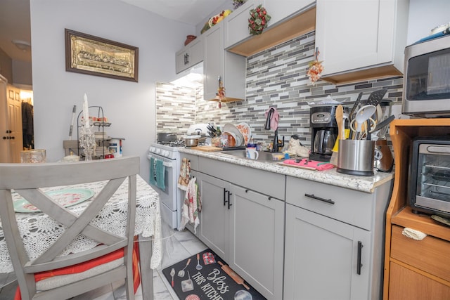 kitchen featuring sink, backsplash, light stone counters, and gas range gas stove