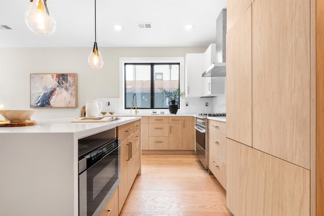 kitchen with wall chimney exhaust hood, light hardwood / wood-style flooring, decorative light fixtures, light brown cabinetry, and high end range