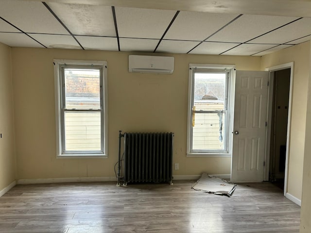 empty room featuring a wall unit AC, radiator, a paneled ceiling, and light wood-type flooring