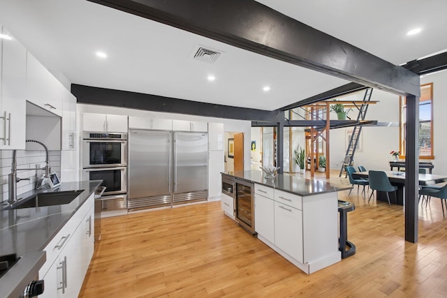 kitchen with dark countertops, appliances with stainless steel finishes, a sink, light wood-style flooring, and wine cooler