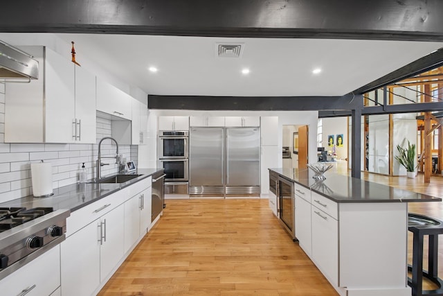 kitchen with dark countertops, appliances with stainless steel finishes, a sink, a kitchen bar, and visible vents
