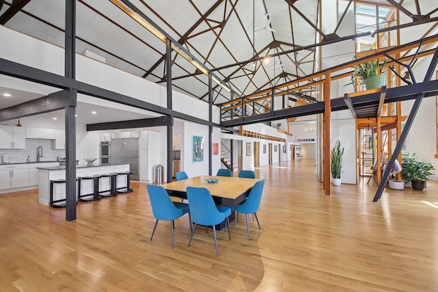 dining area with light wood-style flooring, stairs, and high vaulted ceiling