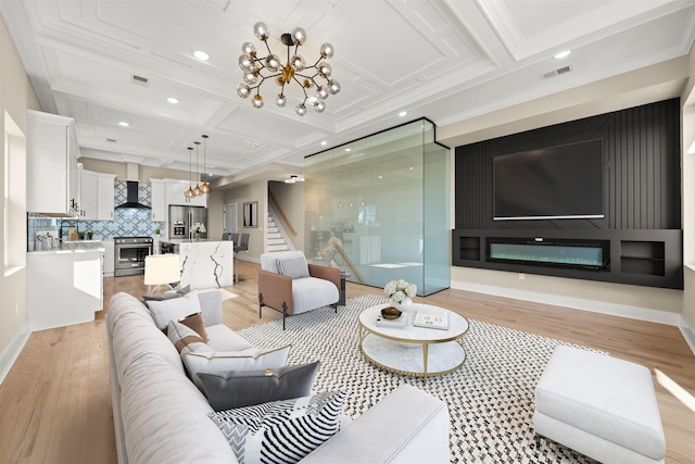 living room featuring an inviting chandelier, visible vents, coffered ceiling, and light wood finished floors