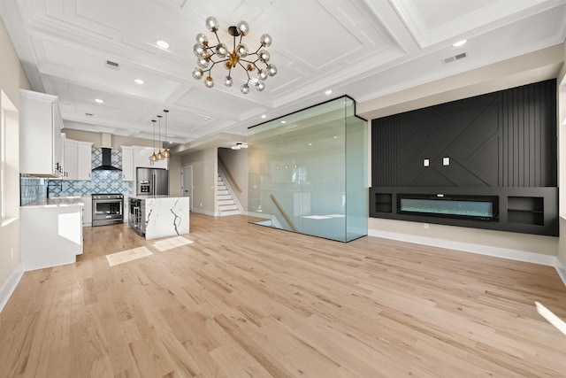 unfurnished living room featuring visible vents, coffered ceiling, stairs, light wood-type flooring, and a chandelier