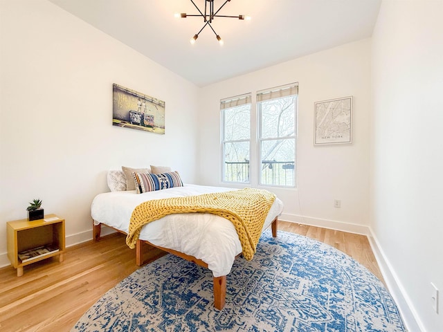 bedroom with baseboards, a notable chandelier, and light wood-style flooring