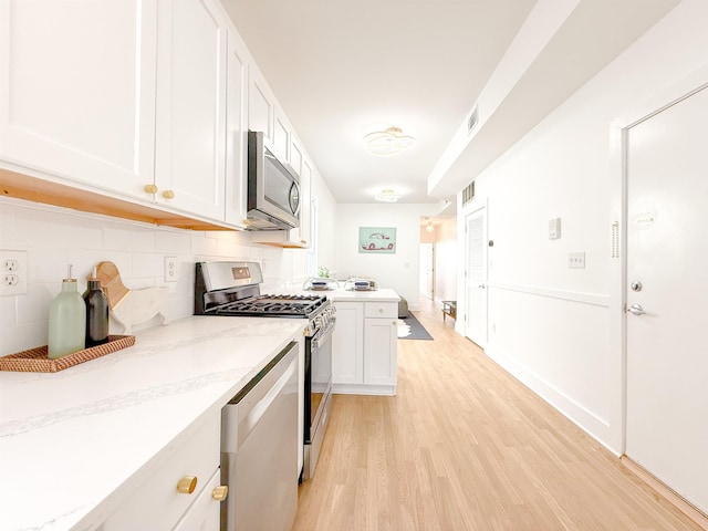 kitchen featuring tasteful backsplash, light wood-type flooring, stainless steel appliances, white cabinets, and visible vents