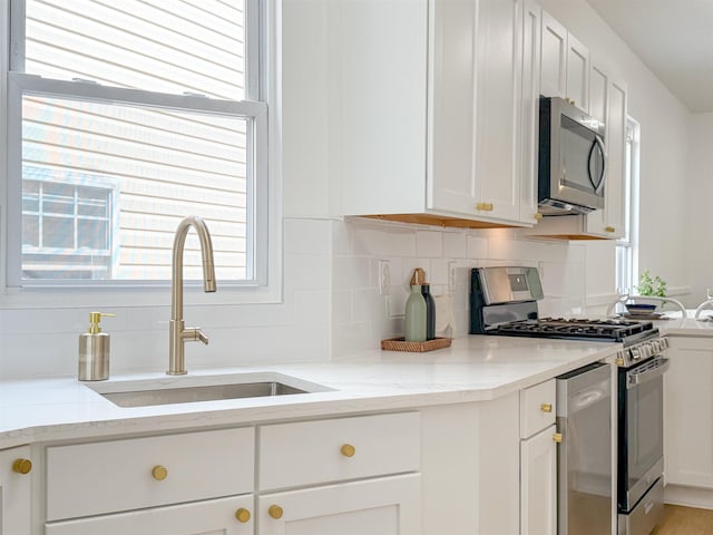 kitchen featuring a sink, plenty of natural light, decorative backsplash, white cabinets, and appliances with stainless steel finishes