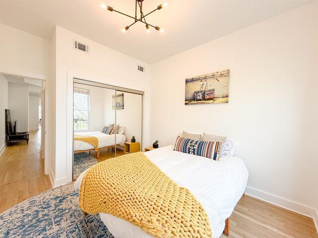 bedroom with light wood-type flooring, baseboards, visible vents, and an inviting chandelier