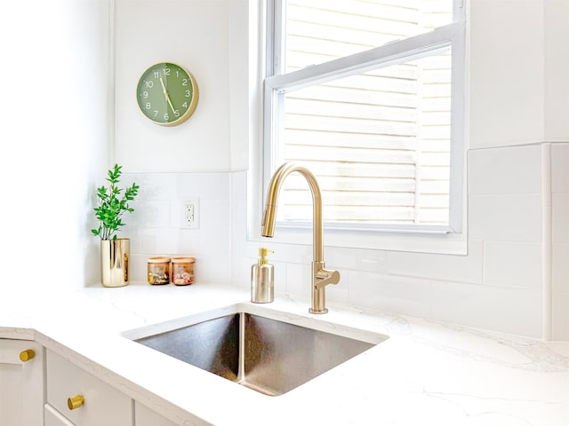 room details with light stone countertops, a sink, backsplash, and white cabinetry