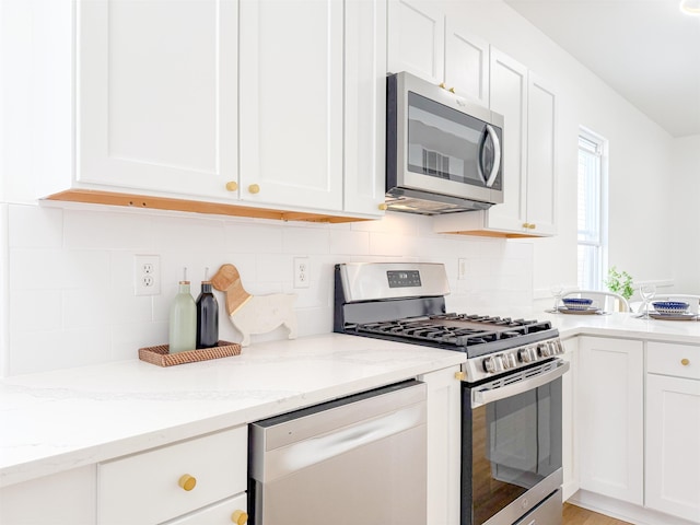 kitchen with white cabinets, backsplash, light stone countertops, and stainless steel appliances