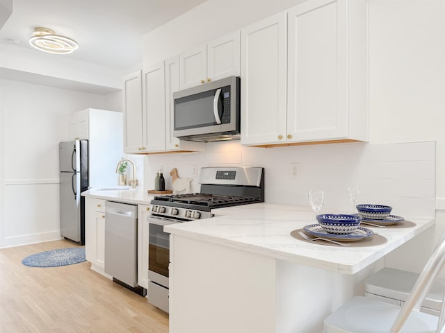 kitchen with tasteful backsplash, stainless steel appliances, light wood finished floors, white cabinetry, and light stone countertops