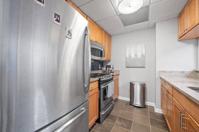 kitchen featuring dark tile patterned flooring, decorative backsplash, stainless steel appliances, light stone countertops, and a drop ceiling