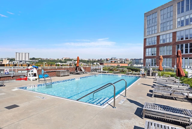 community pool featuring a city view, a patio area, and fence