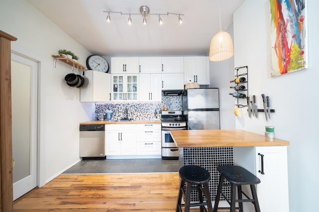 kitchen with wooden counters, a kitchen bar, stainless steel appliances, and white cabinets