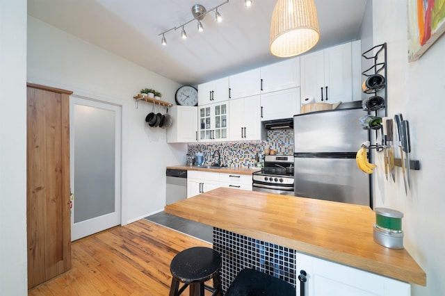 kitchen with pendant lighting, backsplash, stainless steel appliances, white cabinets, and wood counters