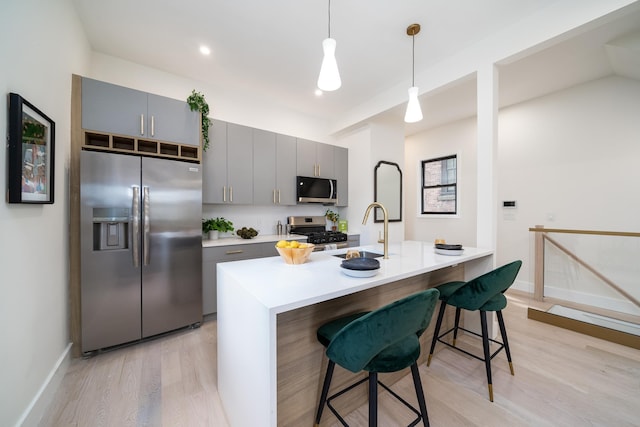 kitchen with gray cabinetry, a breakfast bar, stainless steel appliances, sink, and hanging light fixtures