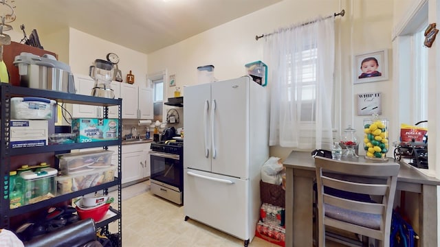 kitchen with white cabinetry, stainless steel gas stove, sink, and white fridge